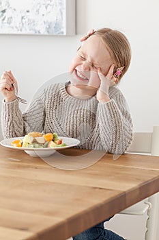 Cute little girl eating a fruit salad in design dining room. Child having a dinner at home. Healthy nutrition for small