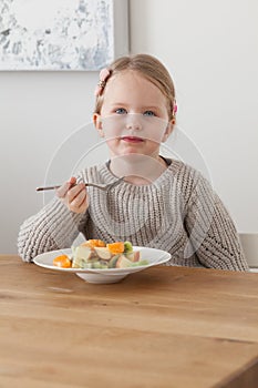 Cute little girl eating a fruit salad in design dining room. Child having a dinner at home. Healthy nutrition for small