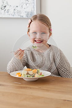 Cute little girl eating a fruit salad in design dining room. Child having a dinner at home. Healthy nutrition for small