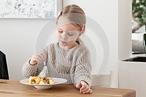 Cute little girl eating a fruit salad in design dining room. Child having a dinner at home. Healthy nutrition for small