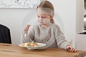 Cute little girl eating a fruit salad in design dining room. Child having a dinner at home. Healthy nutrition for small