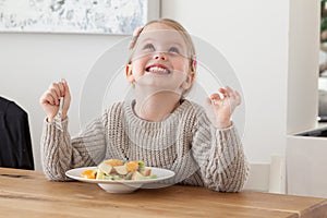 Cute little girl eating a fruit salad in design dining room. Child having a dinner at home. Healthy nutrition for small