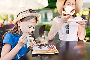 Cute little girl eating a piece of waffles with whipped cream, strawberries and blueberries with her sister