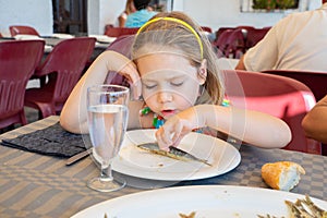 Cute little girl eating a sardine cooked in a white dish in restaurant