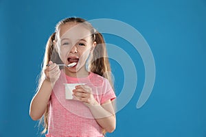 Cute little girl eating tasty yogurt on background. Space for text