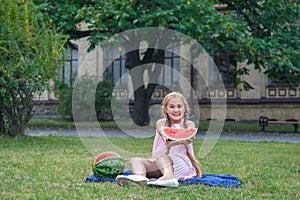 Cute little girl eating watermelon on the grass in summer time. with ponytail long hair and toothy smile sitting on grass and enjo