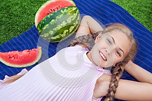 Cute little girl eating watermelon on the grass in summer time. with ponytail long hair and toothy smile sitting on grass and enjo