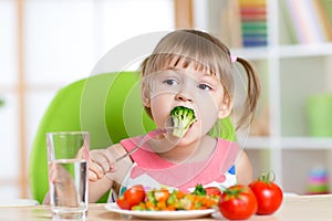 Cute little girl eats vegetable salad using fork