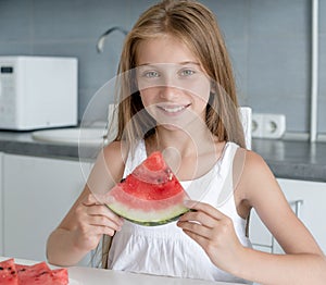 Cute little girl eats a watermelon in the kitchen