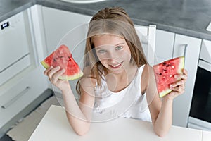 Cute little girl eats a watermelon in the kitchen