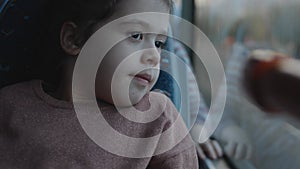 A cute little girl is enjoying the ride by bus. Looking through bus window.