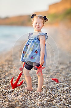 Cute little girl enjoying summer time on sea side beach happy playing with red star and tiny toy anchor on sand wearing nobby