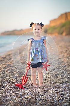 Cute little girl enjoying summer time on sea side beach happy playing with red star and tiny toy anchor on sand wearing nobby
