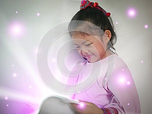 Cute little girl enjoys reading a magic book with light rays shining bright from  - read and education for a child