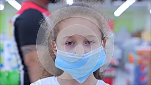 Cute little girl from an epidemic of coronaviruses or viruses looks at the camera amid masked people from the virus who