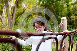 Cute little girl in eyeglasses climbing on a rope bridge