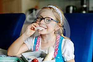 Cute Little Girl with Eyeglasses Eating Sandwich and Fruits during Break between Classes. Healthy Unhealthy Food for Kid