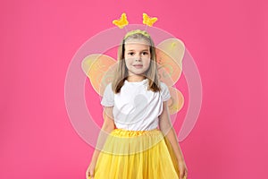 Cute little girl in fairy costume with yellow wings on pink background