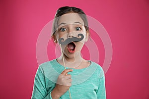 Cute little girl with fake mustache on pink background