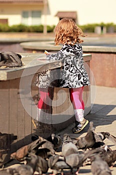 Cute little girl feeding doves with bread crumbs