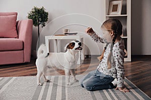Cute little girl feeding her dog at home. Childhood pet
