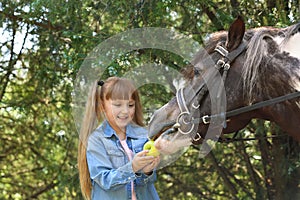Cute little girl feeding her pony with apple
