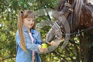 Cute little girl feeding her pony with apple