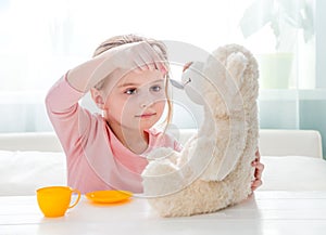 Cute little girl feeding toy teddy bear