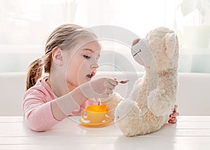 Cute little girl feeding toy teddy bear