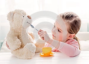 Cute little girl feeding toy teddy bear