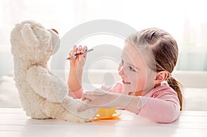 Cute little girl feeding toy teddy bear