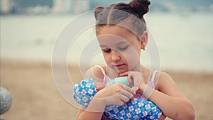 Cute little girl feeds her favorite doll from a toy bottle. Little child playing with doll in the park by the sea. happy