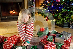 Cute little girl feeling unhappy with her Christmas gifts. Child sitting by a fireplace in a cozy dark living room on Xmas eve.