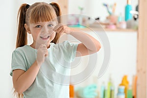 Cute little girl flossing her teeth in bathroom