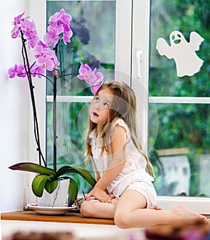 Cute little girl with flower sitting on windowsill of new pvc wi