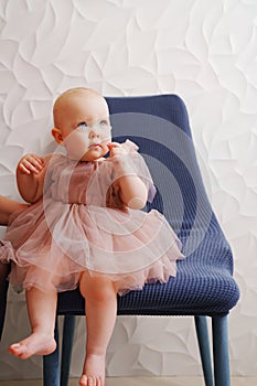 Cute little girl in a fluffy fancy pink dress sitting on a blue chair.