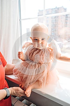 Cute little girl in a fluffy fancy pink dress sitting on the windowsill