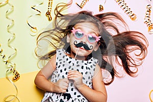 Cute little girl in funny glasses with paper mustache.