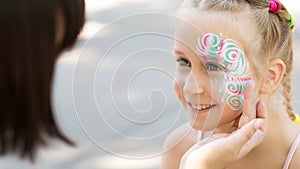 Cute little girl getting her face painted in park photo