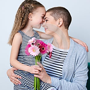 Cute little girl giving mom bouquet of pink gerbera daisies. Loving mother and daughter smiling and hugging.