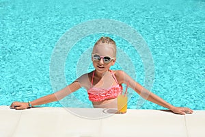 Cute little girl with glass of juice at swimming pool edge on sunny day