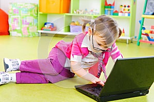 Cute little girl in glasses with laptop on floor