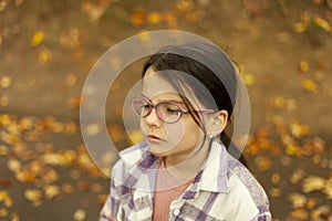 Cute little girl in glasses and plaid shirt in autumn park