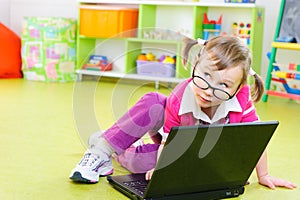 Cute little girl in glasses with laptop on floor