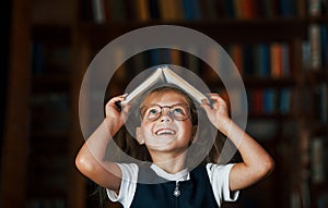 Cute little girl in glasses stands in the library full of books. Conception of education