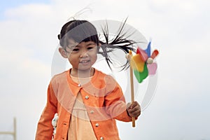 Cute little girl on grass in summer day holds windmill