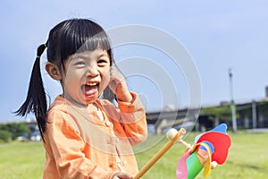 Cute little girl on grass in summer day holds windmill