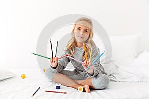 Cute little girl in gray pajamas showing her colorful pencils, l