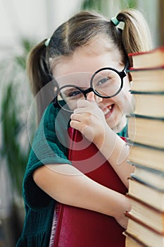 Cute little girl in green dress with red book in her hands fixing a glasses on her nose. Reading and education concept