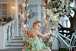 Cute little girl in a green dress sitting on swings decorated wi